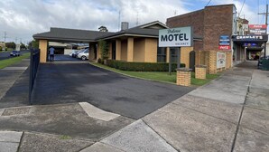 Un motel con un cartel que indica disponibilidad, un estacionamiento y una fachada con un letrero que dice 'Crawley's Milk Bar'.