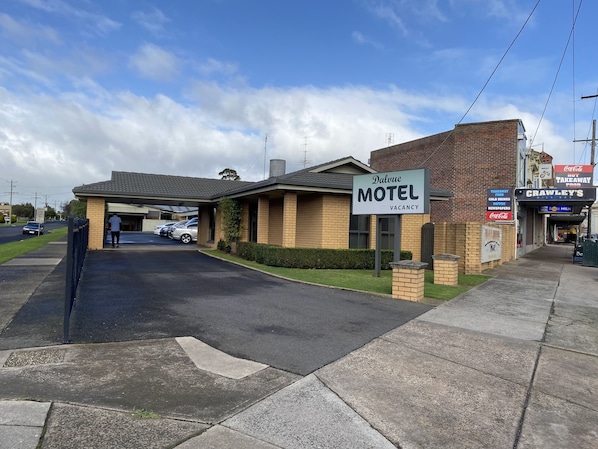 Et motel med et skilt der angiver ledige værelser, en parkeringsplads og en facade med skiltet 'Crawley's Milk Bar'.