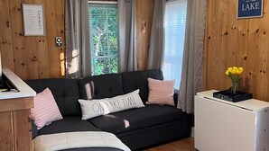 A cozy room with a wooden wall, a black sofa, a white dresser, and a small wooden stool.