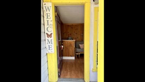 A wooden interior with a 'WELCOME' sign, a small stool, and a couch.