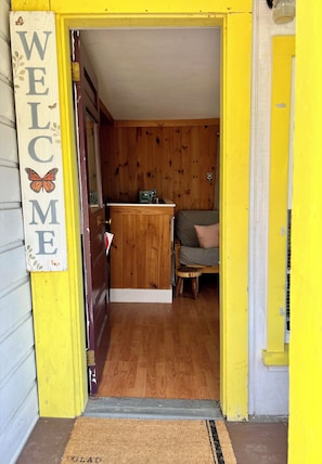 A wooden interior with a 'WELCOME' sign, a small stool, and a couch.
