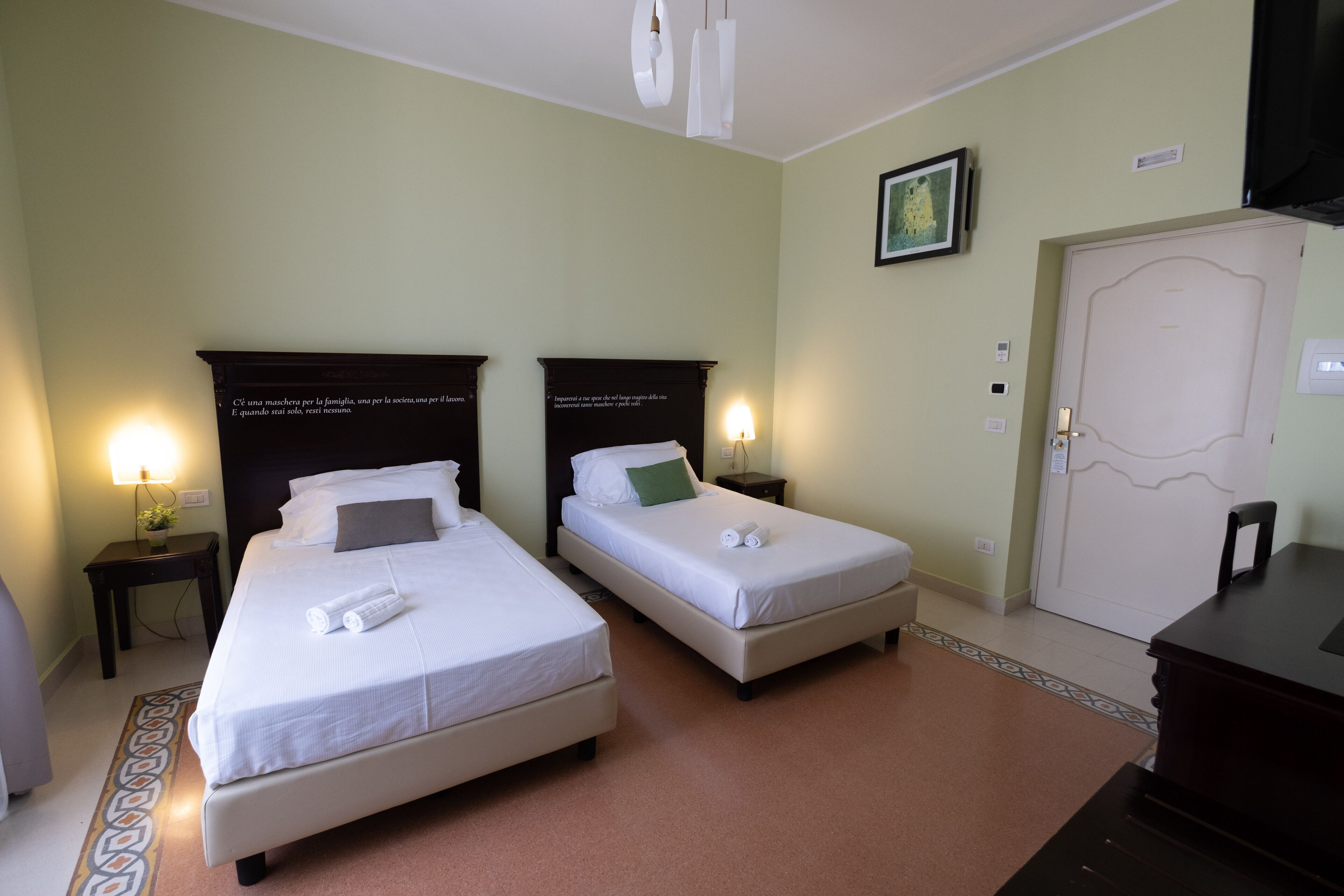A hotel room with two single beds, a desk, a chair, a TV, and a door.