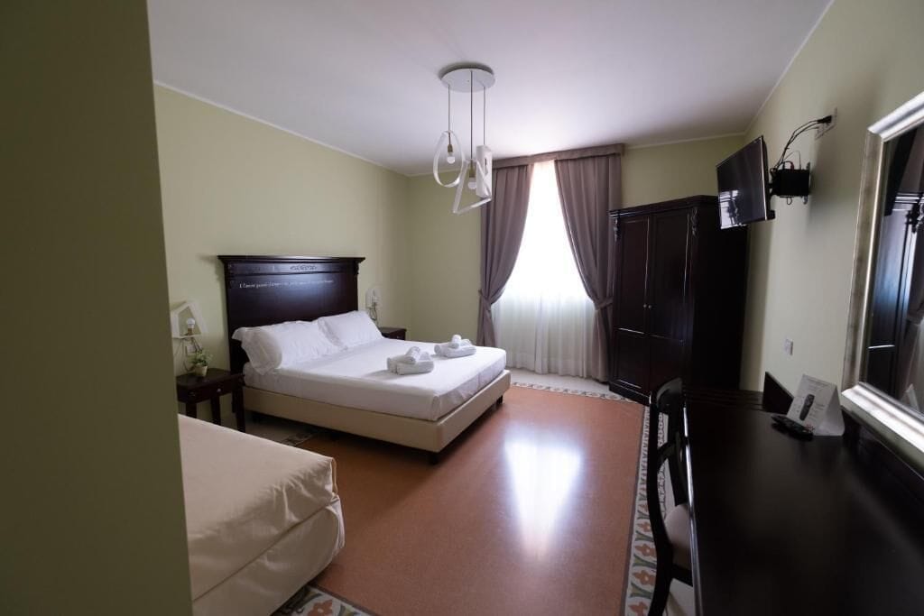 Une chambre d’hôtel avec un lit, un bureau, une chaise, une télévision et une fenêtre avec des rideaux.