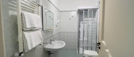 A bathroom with a glass shower enclosure, a sink, a toilet, and a towel rack with multiple towels.