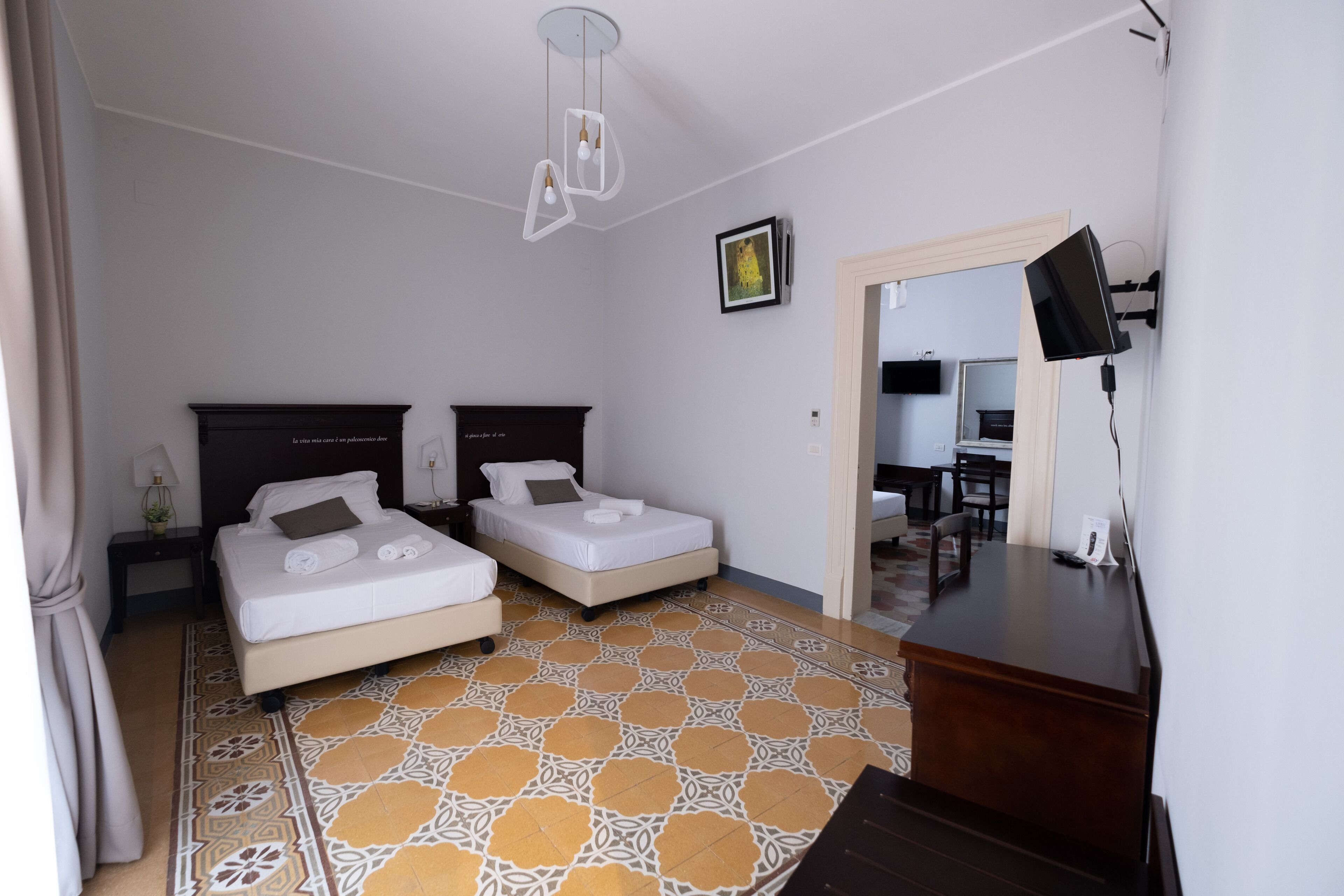 A hotel room with two beds, a desk, a chair, a TV, and a patterned floor.