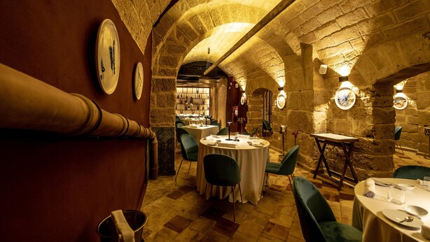 An interior with stone arches, round tables, and green chairs. - Borgo di Ciàula (Santa Flavia)