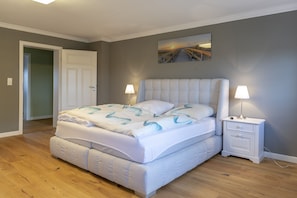 Ein Schlafzimmer mit einem großen Bett, zwei Nachttischen mit Lampen, einer Tür und einem Bild an der Wand.