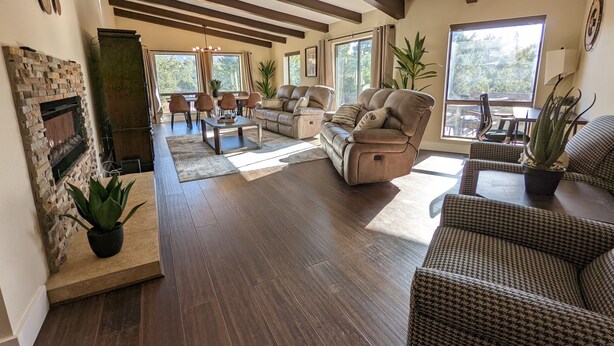 A spacious living room with a fireplace, leather sofa, and large windows offering a view of the outdoors. - Sedona 4BR • Red Rock Views • Deck + Game Room (Sedona)