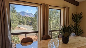 A dining area with a large window offering a view of a road and mountains. - Sedona 4BR • Red Rock Views • Deck + Game Room (Sedona)