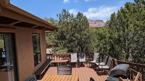 A wooden deck with outdoor seating, overlooking a forested area and a mountain in the distance. - Sedona 4BR • Red Rock Views • Deck + Game Room (Sedona)
