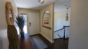 A hallway with a wooden floor, a white door, a potted plant, a textured rug, and a staircase with a railing. - Sedona 4BR • Red Rock Views • Deck + Game Room (Sedona)