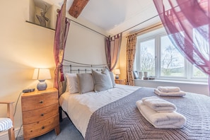 Quarto com cama, mesas de cabeceira, cômoda de madeira e janela com cortinas.