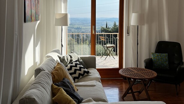 A living room with a sofa, a round table, and a chair. There is a balcony with a view of the landscape. - Private garden, tranquility and privacy (San Michele-montecchio)