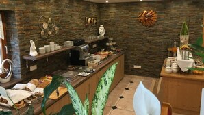 A modern breakfast bar with a stone wall backdrop, a coffee machine, and various breakfast items. - Four-bed room with bath, WC - B&B - Golf- und Skipension Krug (Haus)