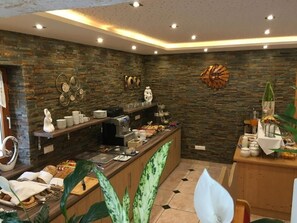 A modern breakfast bar with a stone wall backdrop, a coffee machine, and various breakfast items. - Four-bed room with bath, WC - B&B - Golf- und Skipension Krug (Haus)