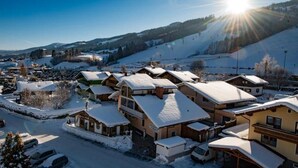 A snow-covered village with traditional chalet-style buildings, a clear sky, and a sunlit landscape. - Four-bed room with bath, WC - B&B - Golf- und Skipension Krug (Haus)