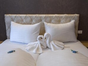 A hotel room with a tufted headboard, two pillows, and two towels arranged on the bed. - Four-bed room with bath, WC - B&B - Golf- und Skipension Krug (Haus)