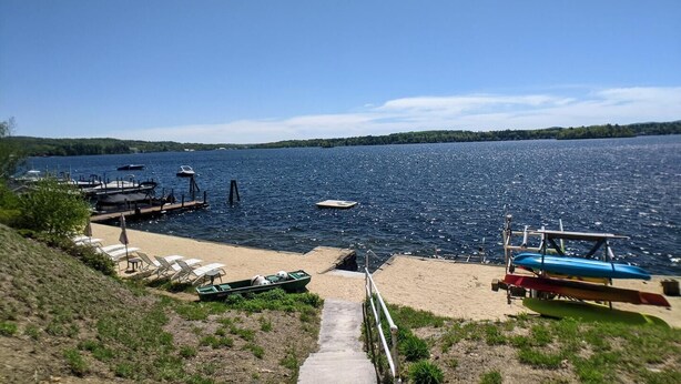 A lakeside dock with boats, a sandy beach, and a clear view of the lake. - Hi Spot Studio with shared beach on Winnipesaukee! (Laconia)