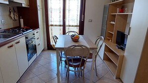 A compact kitchen with a dining table, chairs, a stove, and a TV. - FURNISHED TWO-ROOM APARTMENT 200 MT FROM THE LIDO OF ALGHERO (Alghero)