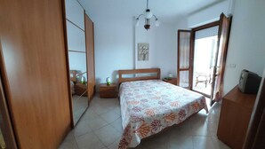 A bedroom with a bed, bedside tables, a mirror, a hanging light fixture, and a window with curtains. - FURNISHED TWO-ROOM APARTMENT 200 MT FROM THE LIDO OF ALGHERO (Alghero)