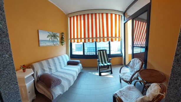 A cozy room with a striped sofa, a small table, and two wicker chairs. - FURNISHED TWO-ROOM APARTMENT 200 MT FROM THE LIDO OF ALGHERO (Alghero)