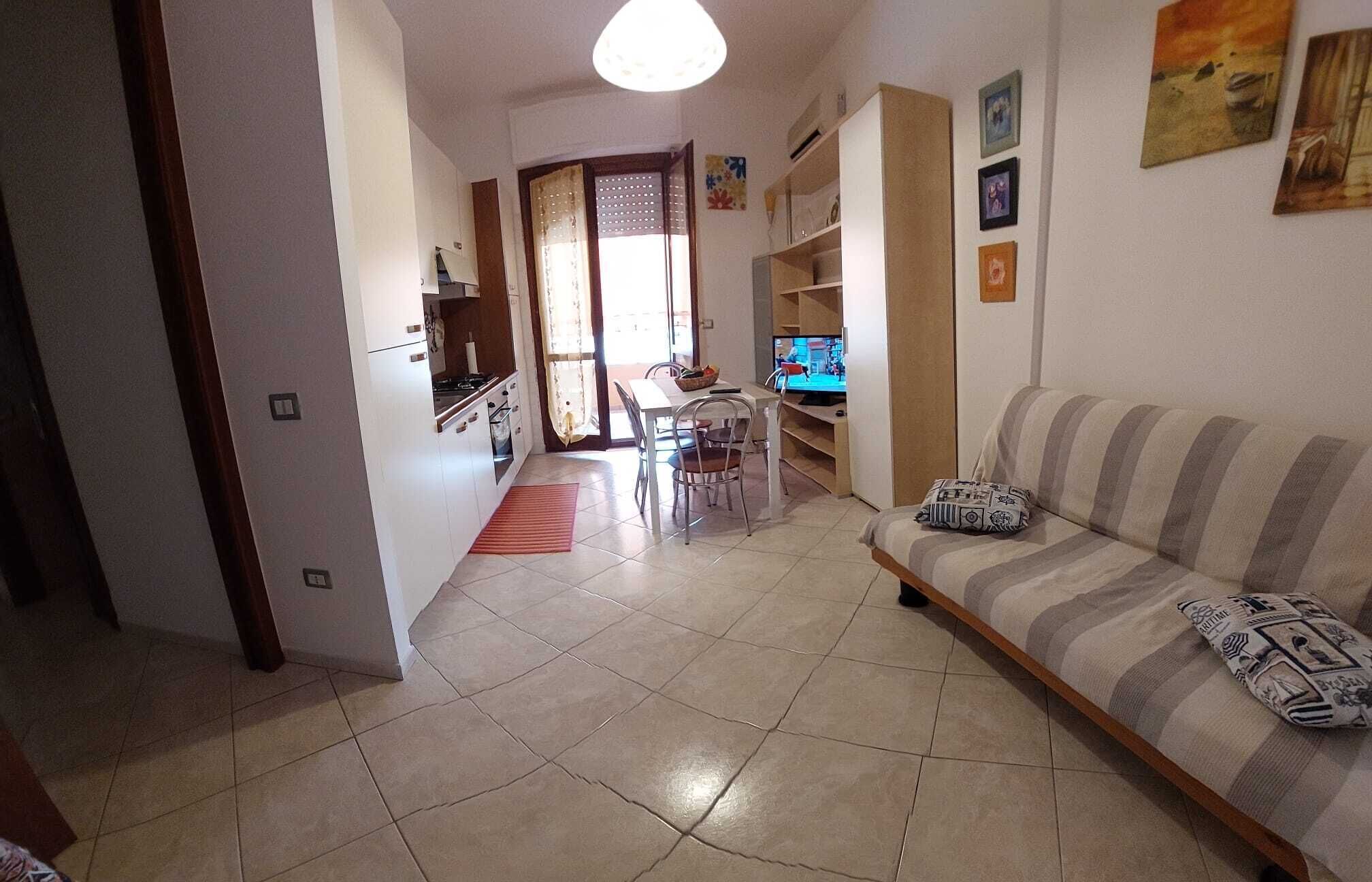 Een woonkamer met een bank, een televisie en een eethoek met een tafel en stoelen.