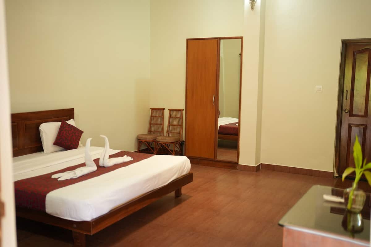 Une chambre d’hôtel avec un lit en bois, un miroir, une armoire et une petite table sur laquelle est posée une plante.