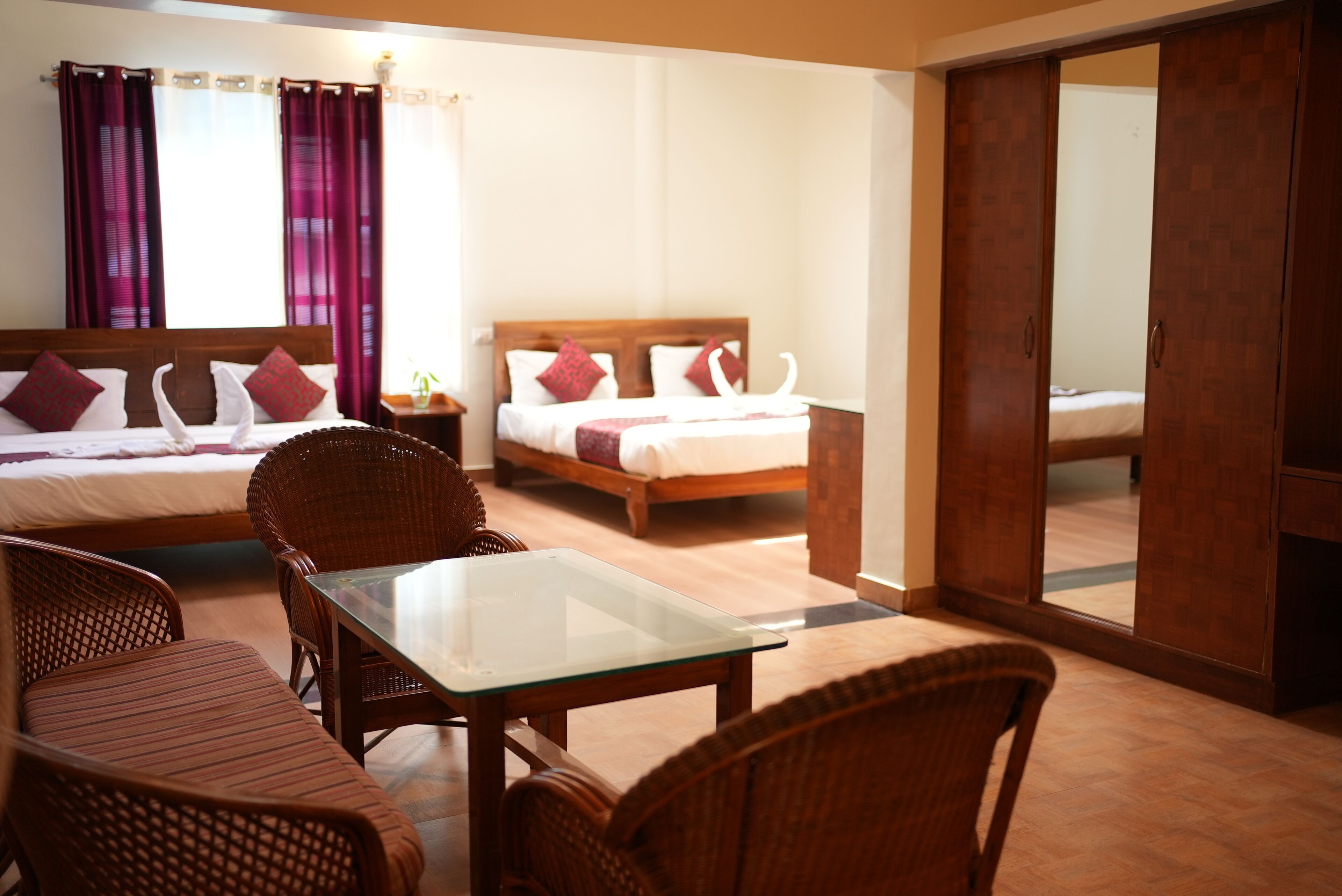 A hotel room with two beds, a dining table, wicker chairs, and a sliding door closet.