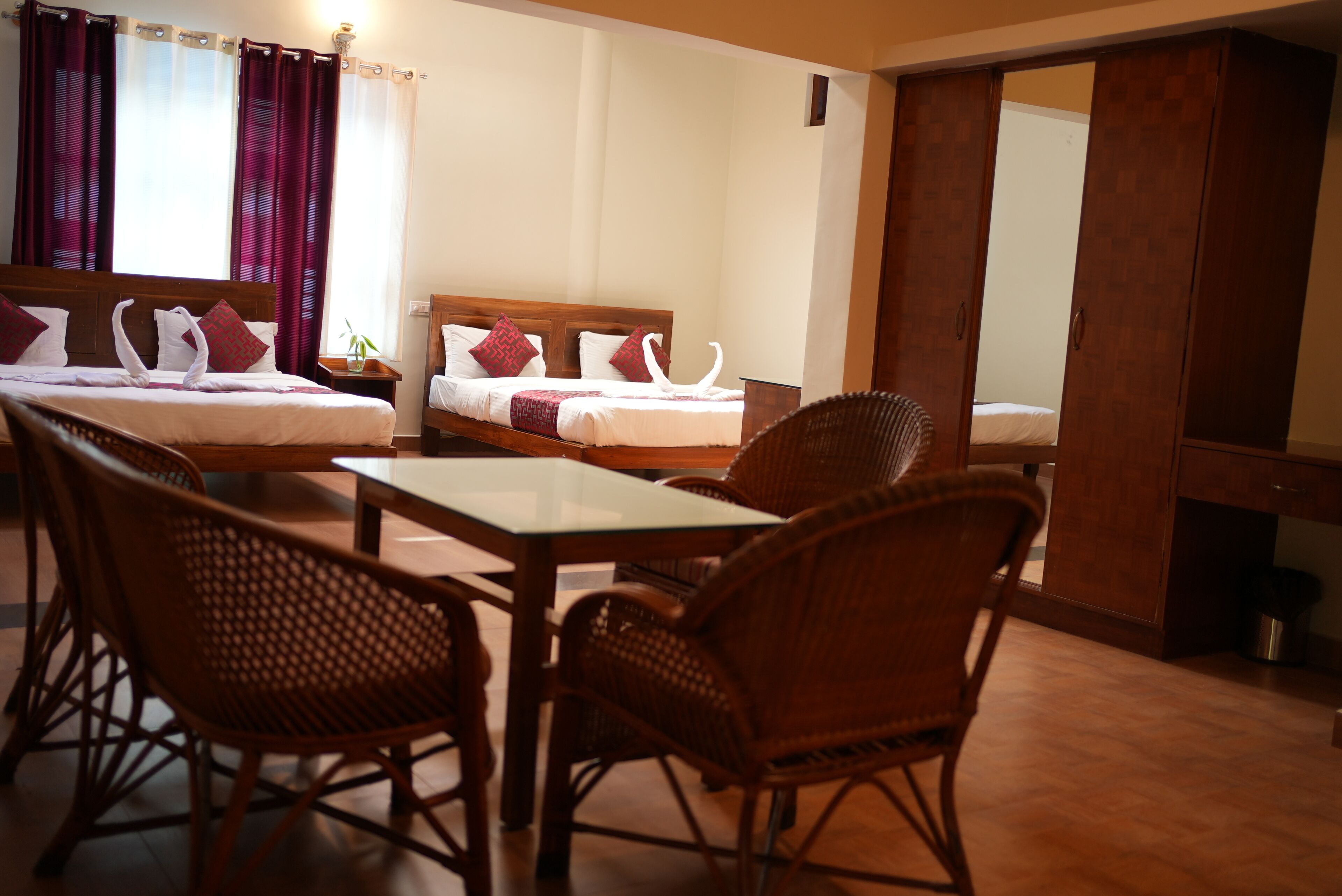 A hotel room with two beds, a dining table, wicker chairs, and a large mirror.