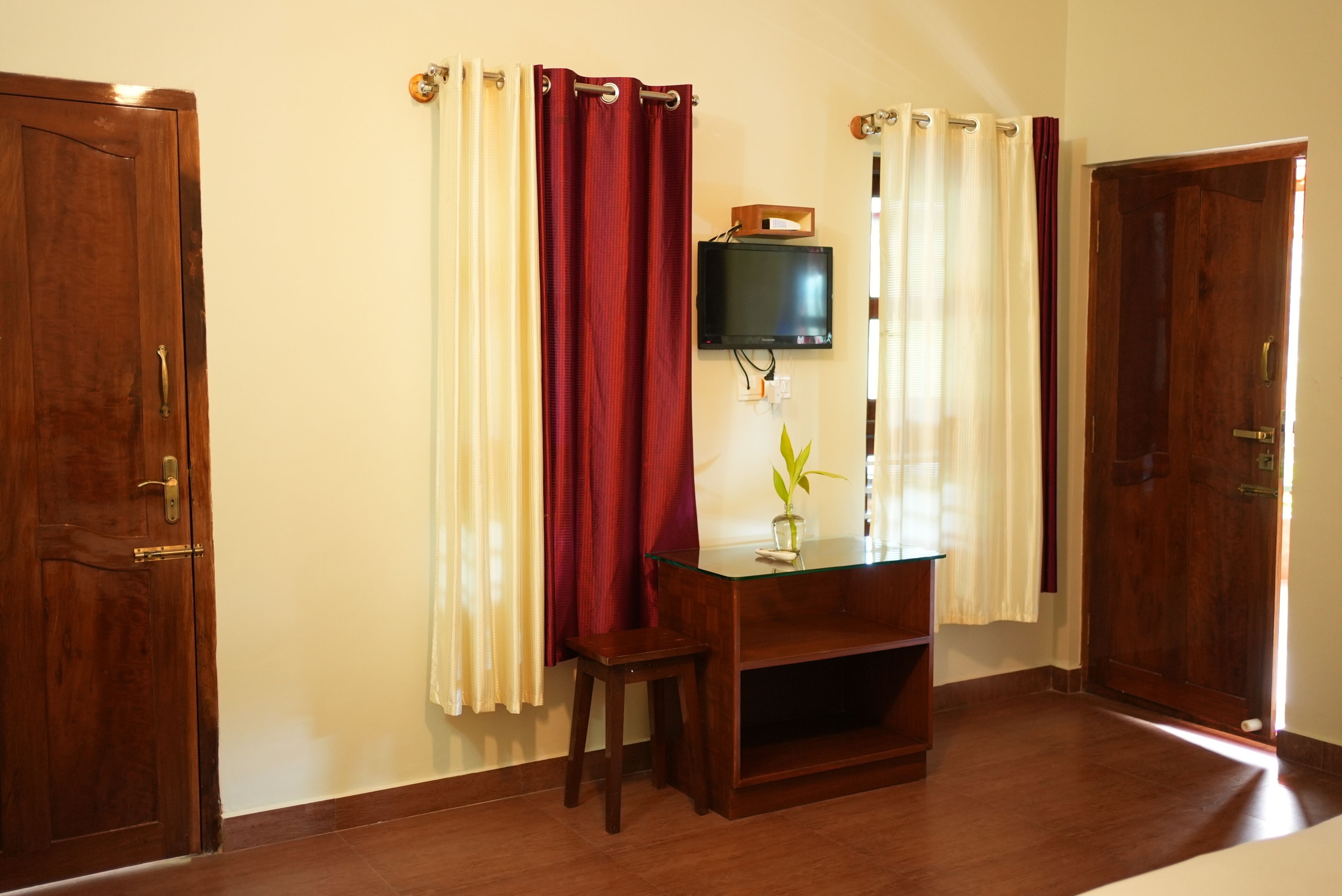 Una habitación con un escritorio de madera, un televisor fijado a la pared y un par de cortinas.