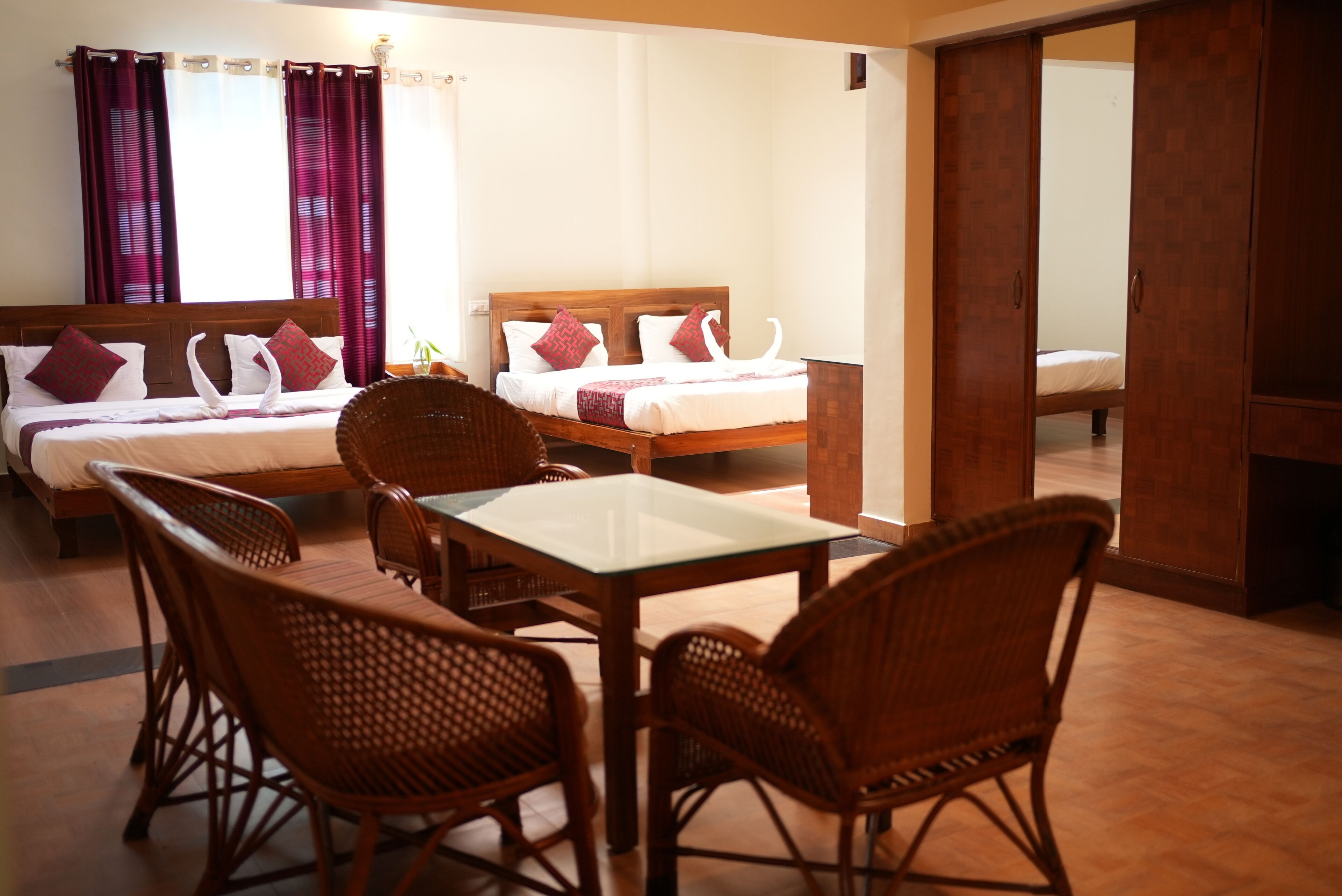 A hotel room with two beds, a dining table, wicker chairs, and a mirror.