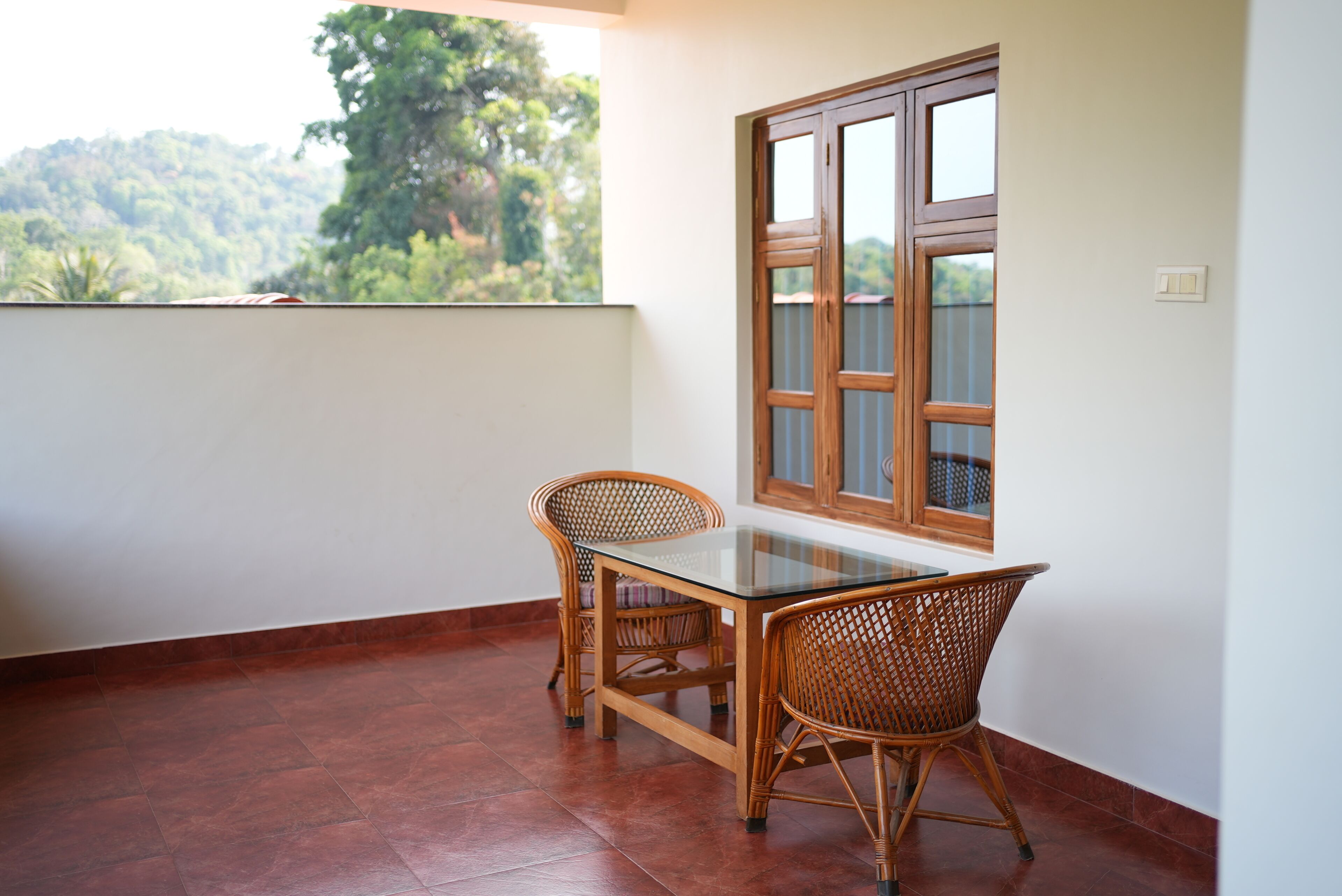 A balcony with a table and chairs, a window, and a view of greenery.