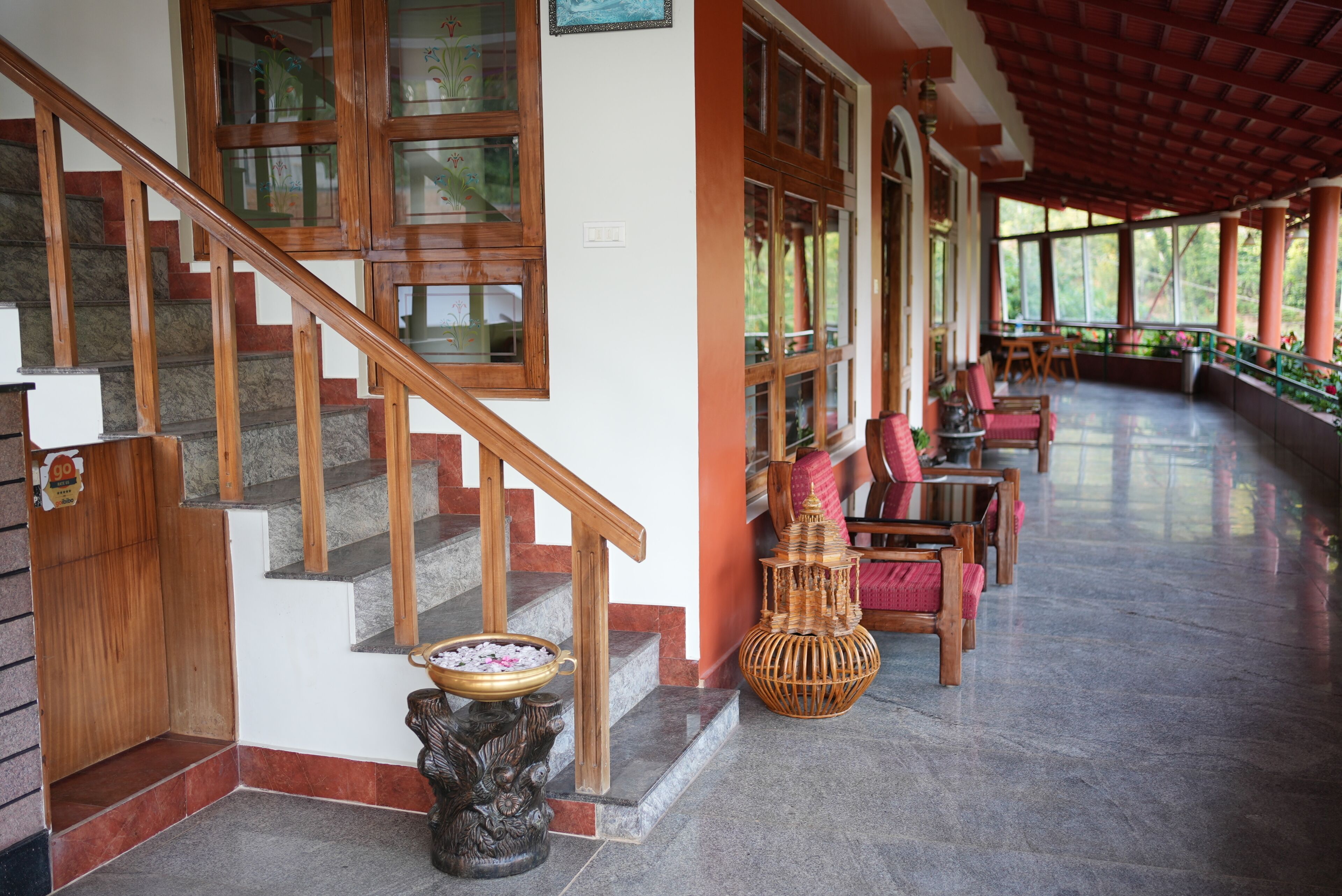 Una escalera con barandillas de madera, un espacio cubierto con sillas y mesas, y un jarrón decorativo.