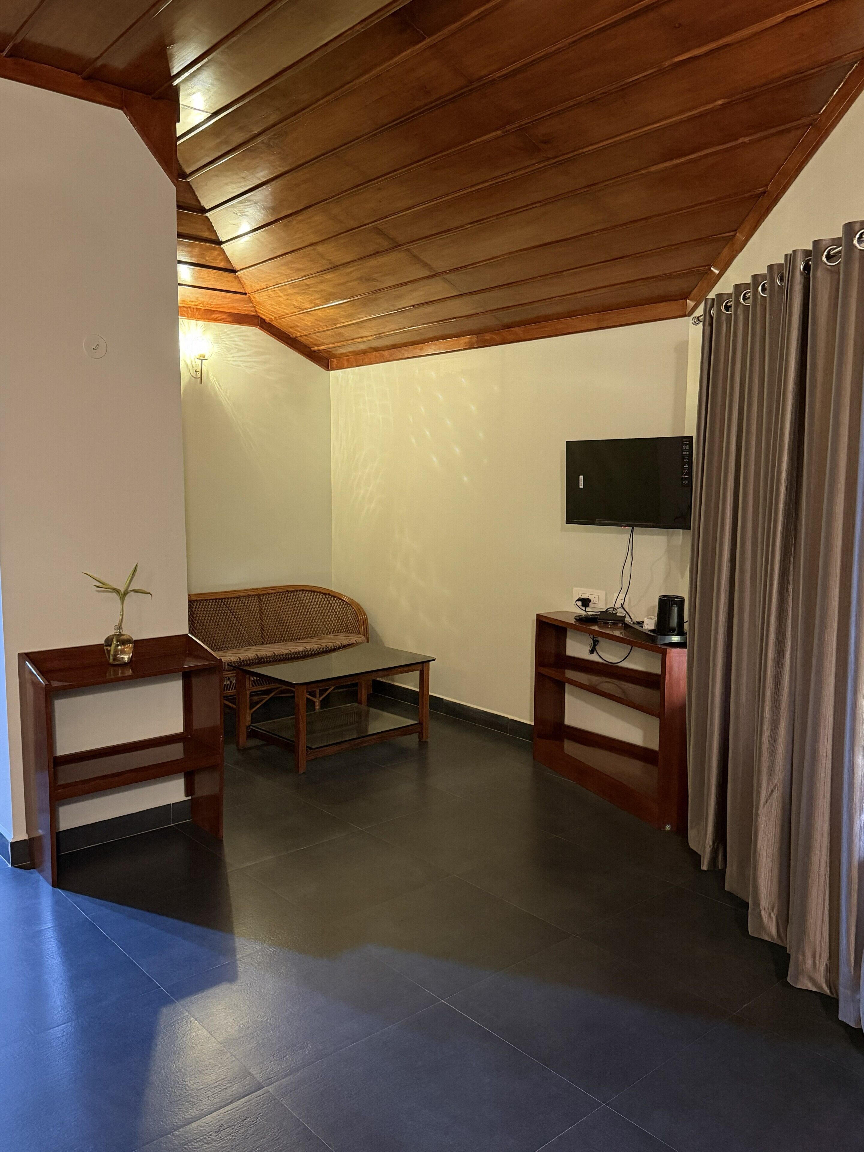 Une pièce avec un plafond en bois, un lit, une télévision, une machine à café et un rideau.