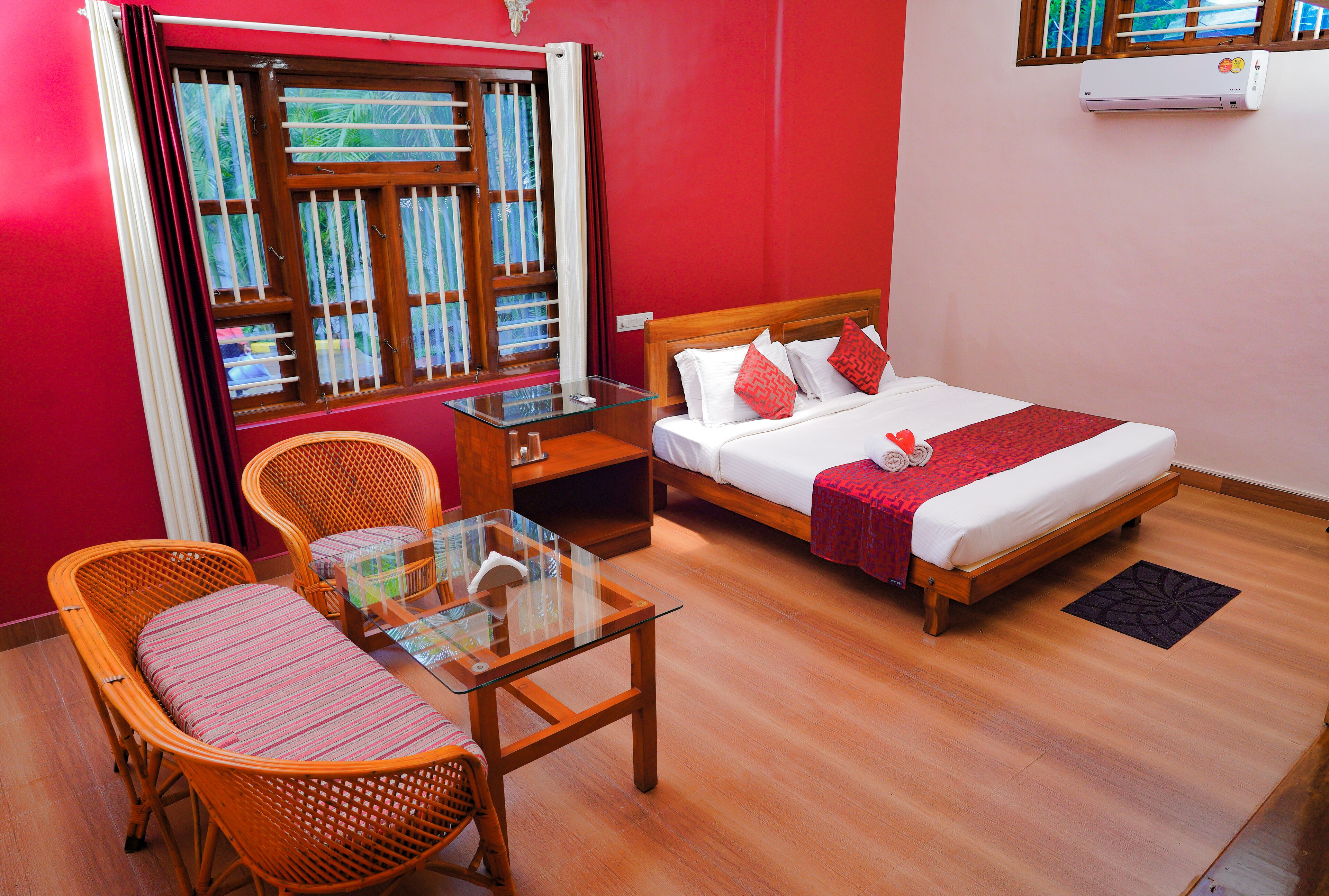 Una habitación de hotel con cama, una mesita de vidrio, sillas de mimbre, una mesita de noche y una ventana con cortinas.