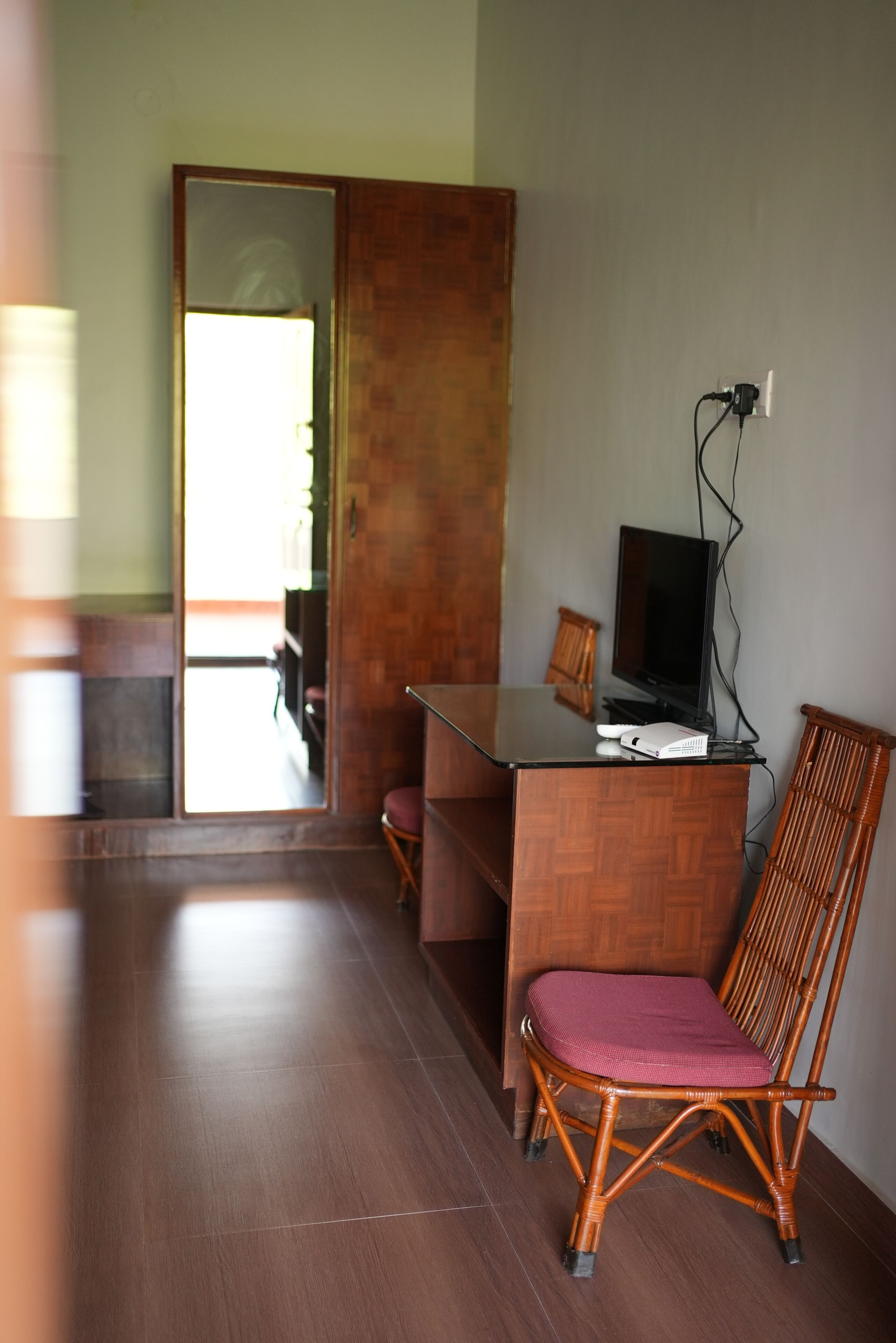A room with a wooden desk, a television, a chair, and a wall socket.