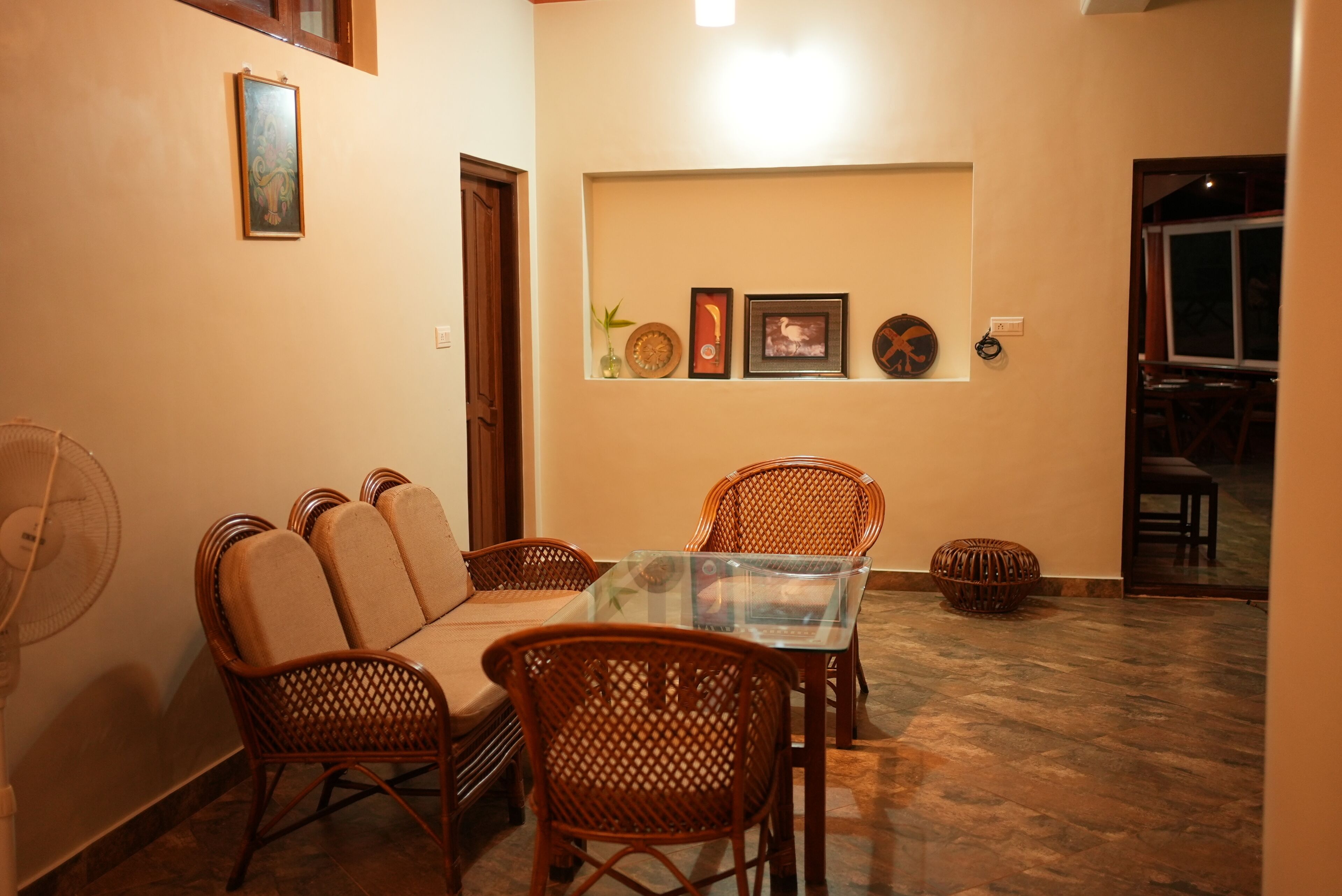 A dining area with wicker chairs, a glass table, and a fan.