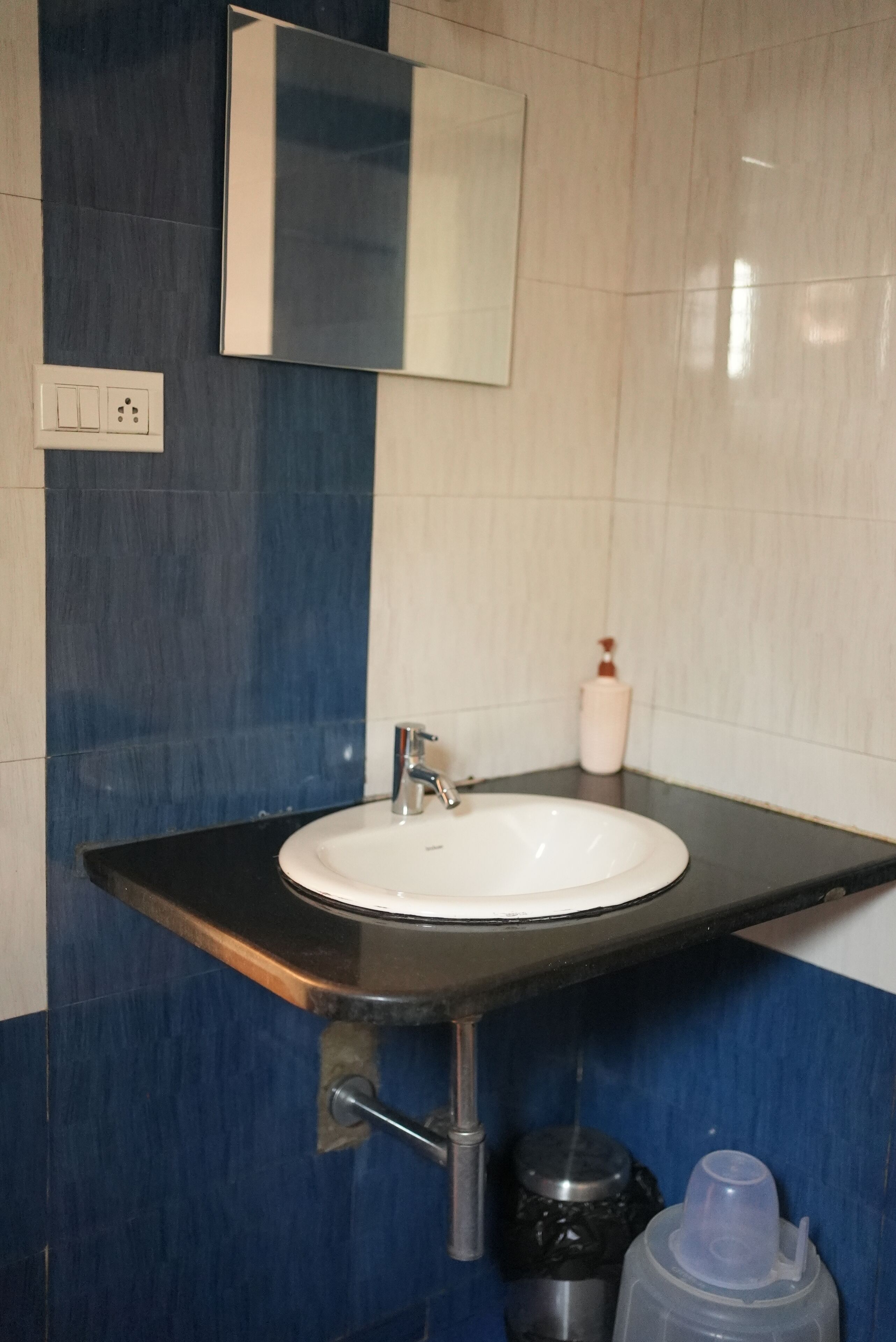 A bathroom with a white sink, a mirror, and a soap dispenser.