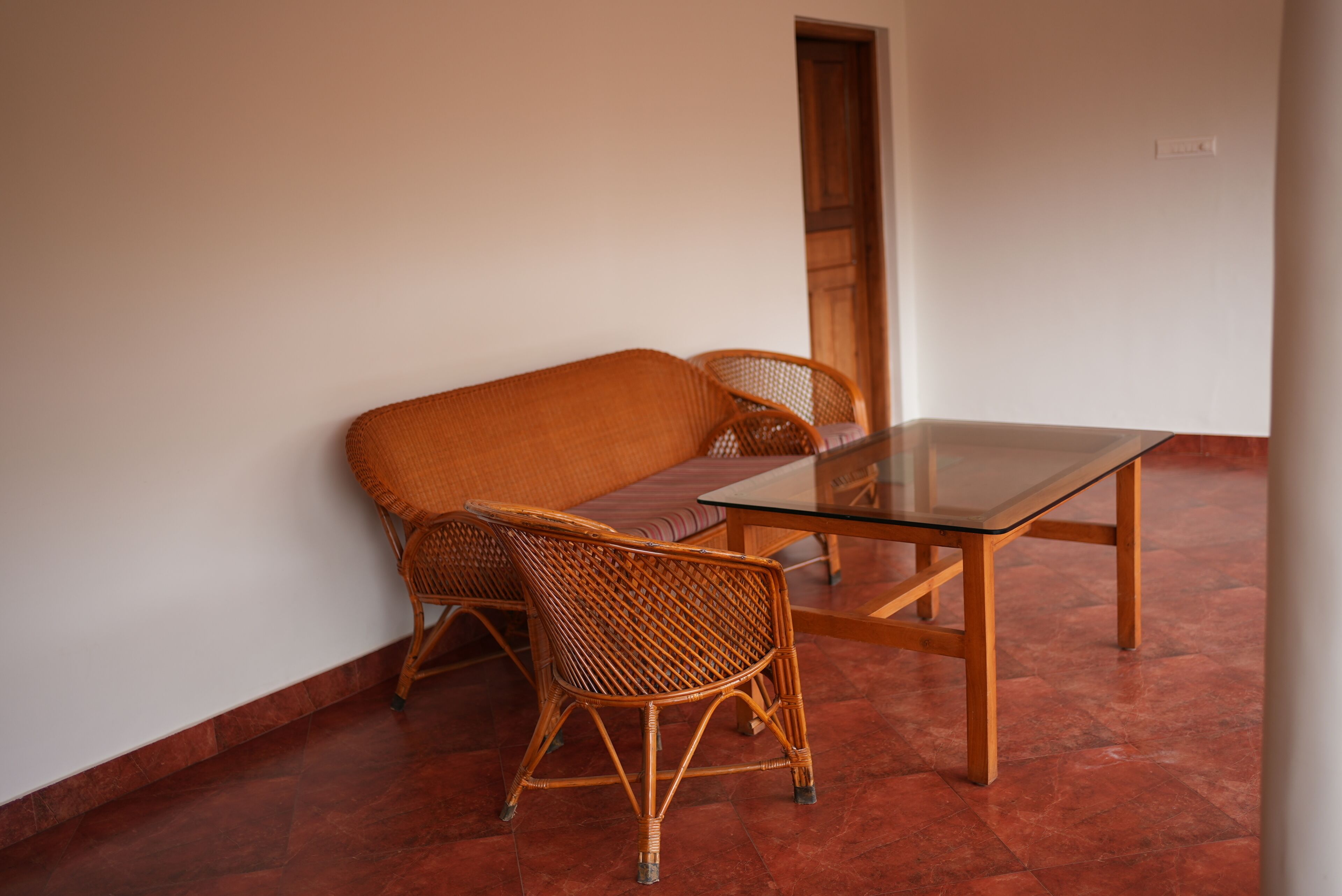 A room with a glass-top table and wicker chairs, a wooden door, and a tiled floor.