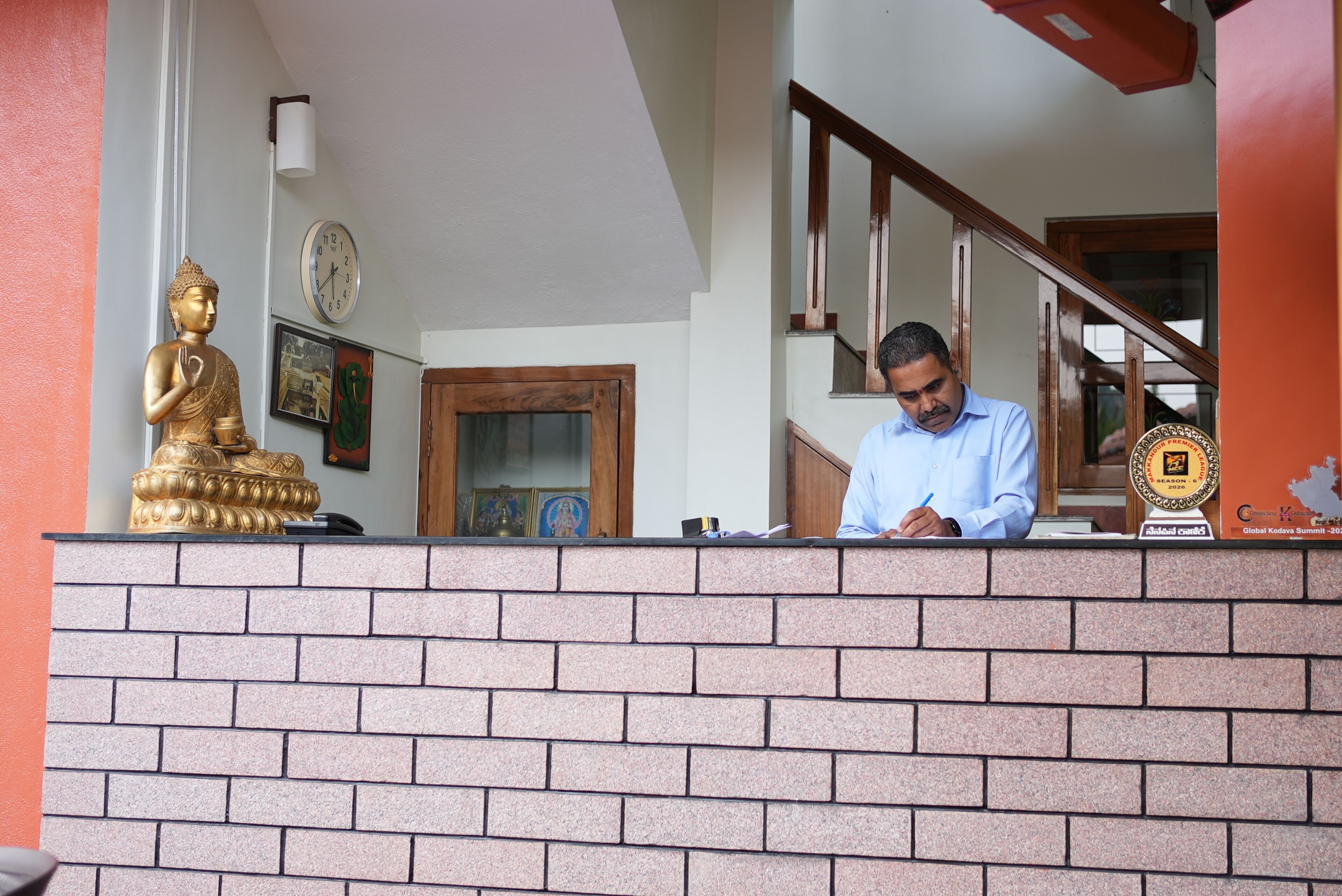 A reception desk with a brick wall, a Buddha statue, a clock, and a framed picture.
