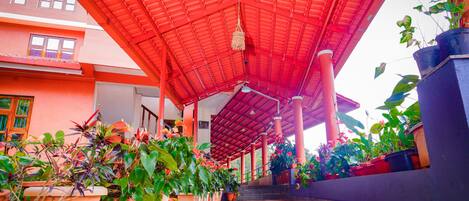 A covered walkway with potted plants and a red roof.