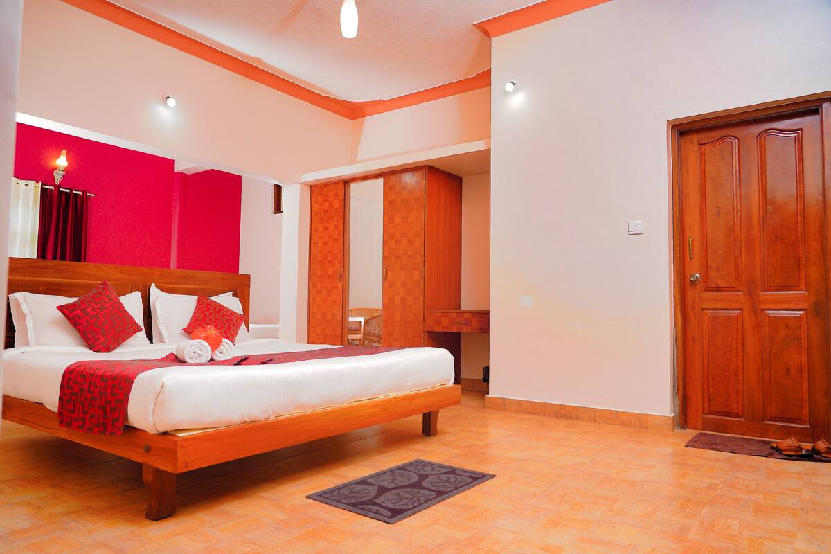 Une chambre avec un lit en bois, un mur d’accent rouge et une armoire en bois.