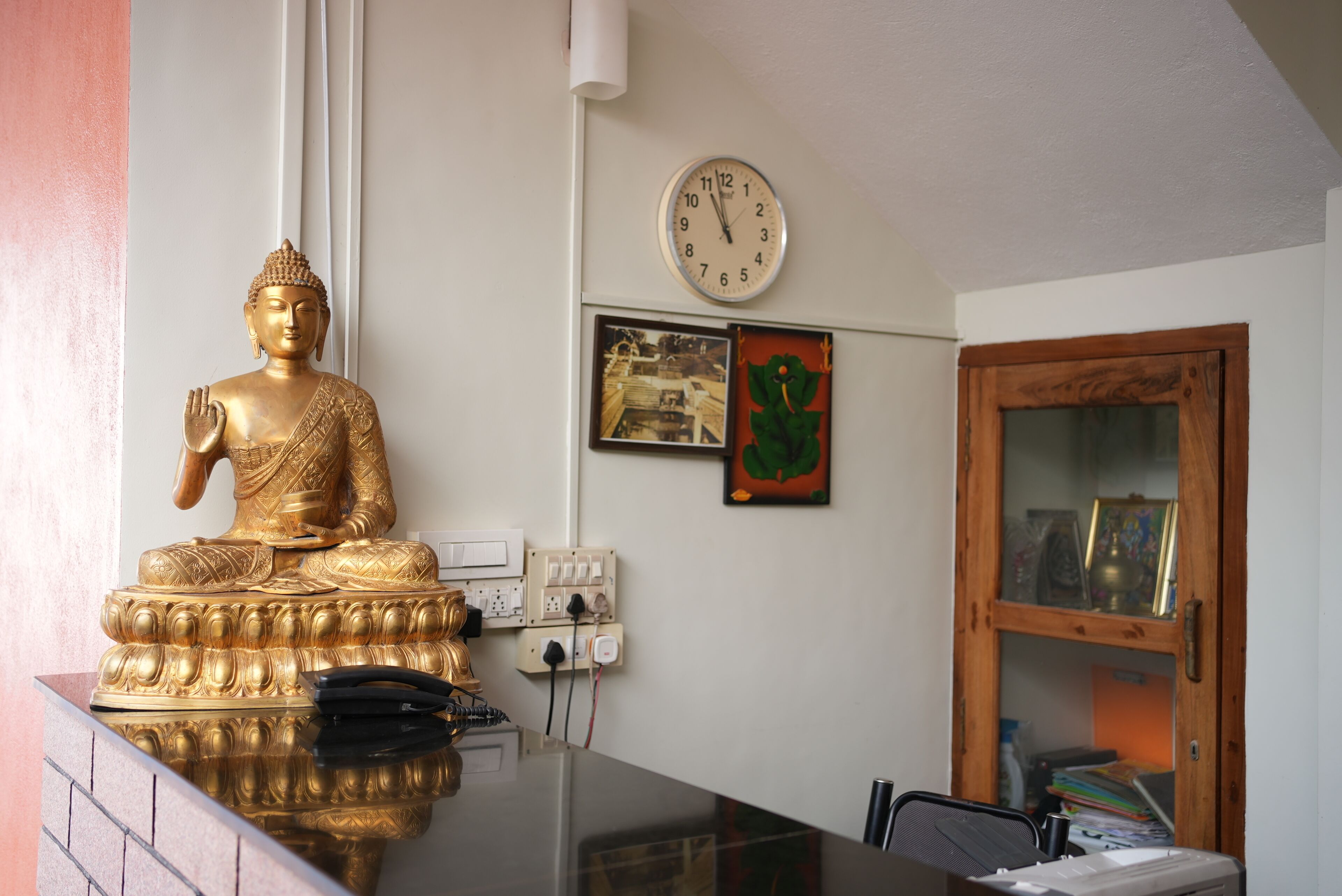 Un área de recepción con una estatua dorada de Buda, un reloj, enchufes, cuadros enmarcados y un mueble de madera.
