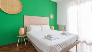 A hotel room with a green wall, a large bed with white bedding, two bedside lamps, and a round woven wall hanging.