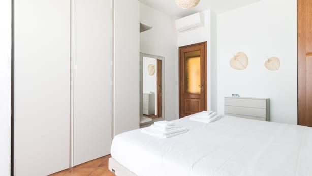 A bedroom with a bed, a bedside table, a mirror, and a door. - Il Borgo Apartments A1 - Sv-d600-bove3ata (Finale Ligure)