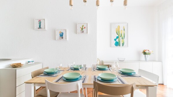 A dining area with a wooden table set for four, white chairs, and framed cactus artwork on the wall.