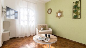 A room with a round table, a chair, a sofa, a wall-mounted mirror, and a framed plant. - Il Borgo Apartments A1 - Sv-d600-bove3ata (Finale Ligure)