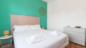 A hotel room with a large bed, a bedside table with a lamp, a dresser, and a decorative wall piece.
