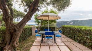 Une terrasse extérieure avec une table et des chaises, un parasol et une vue sur la mer.