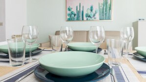 Une table à manger dressée avec de la vaisselle verte et des verres transparents, un canapé beige et un tableau représentant un cactus accroché au mur.